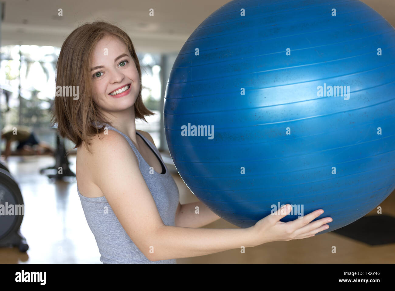 Lächelnden jungen kaukasischen Frau Mädchen mit einem blauen Gymnastikball im Fitnessstudio, Training oder Yoga Pilates Übung Stockfoto