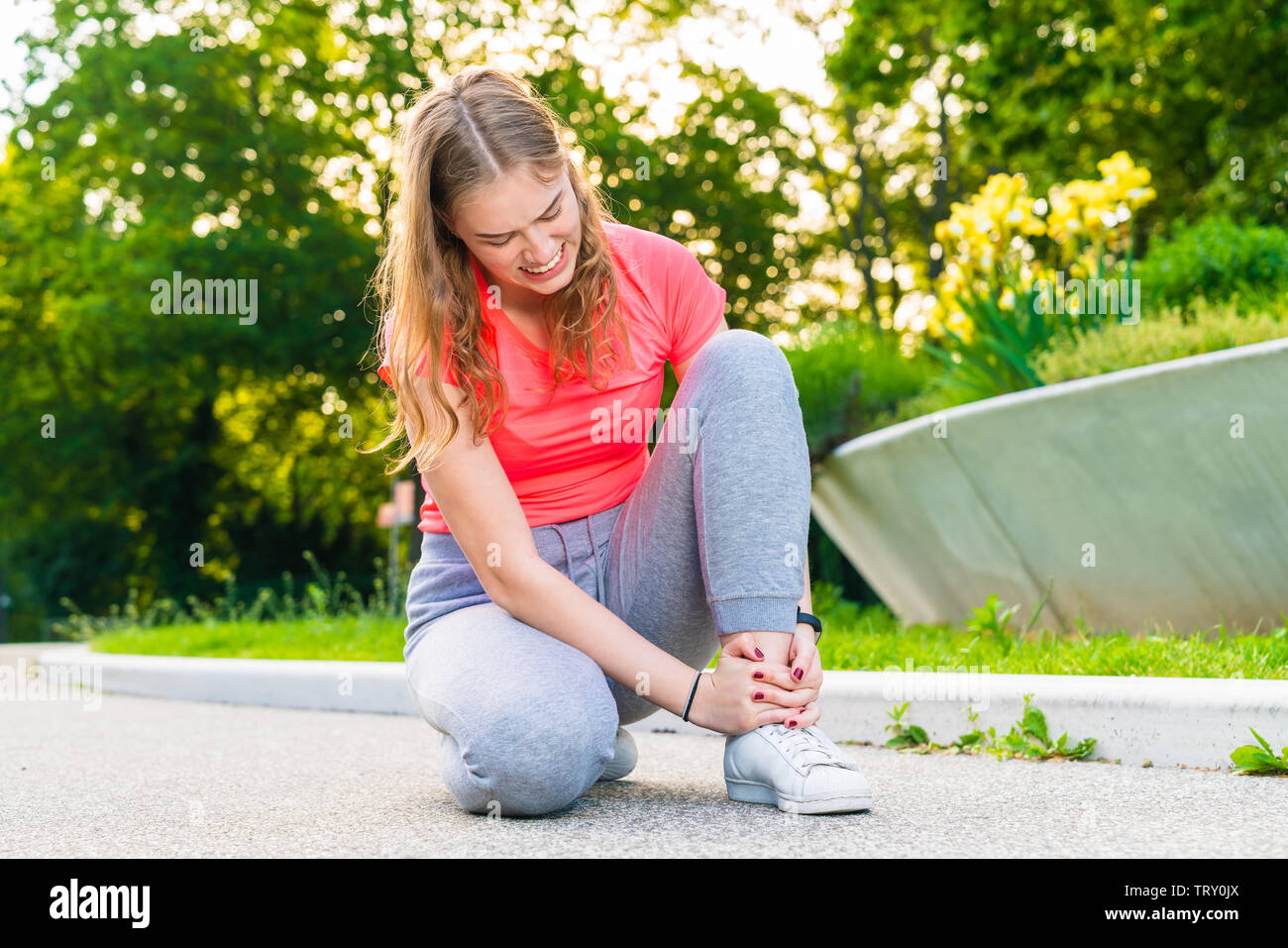 Eine junge joggerin hat ihren Knöchel beim Sport verletzt und hält es fest Stockfoto