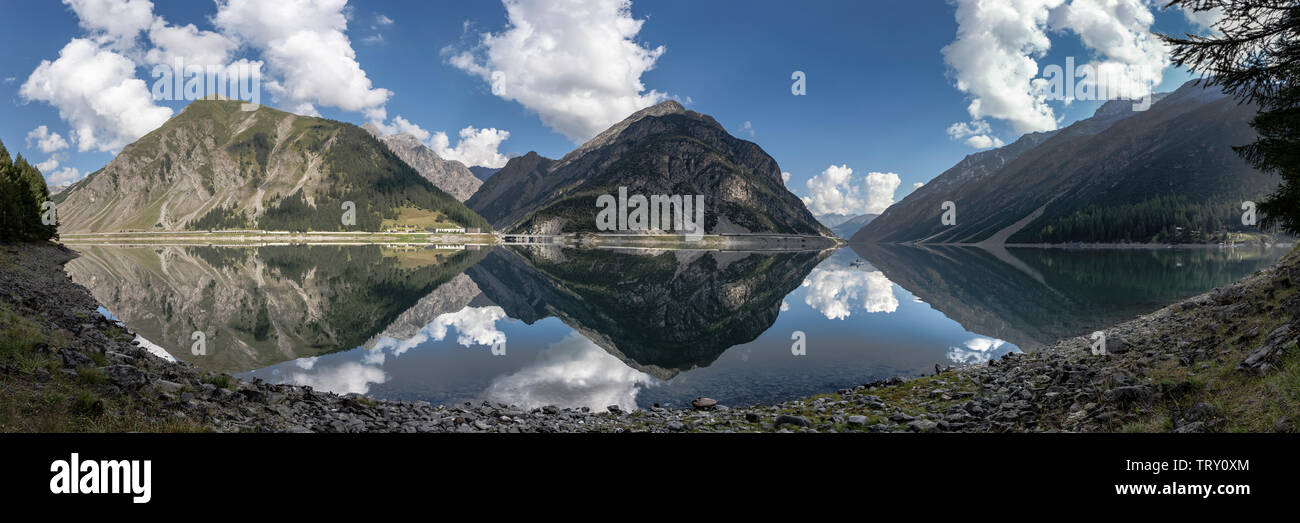 Breites Panorama Landschaft in den Alpen mit einem See, Boot, kaltes Wasser, Reflexionen von einem blauen Himmel und Wolken. Stockfoto