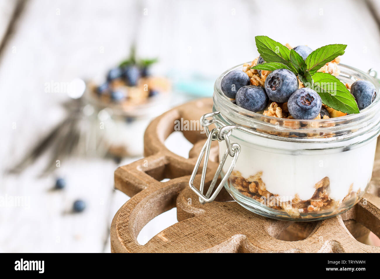 Gesundes Frühstück der Blaubeere parfaits mit frischem Obst, Joghurt, Müsli und Minze über einen rustikalen Kuchen stehen. Selektive konzentrieren. Stockfoto