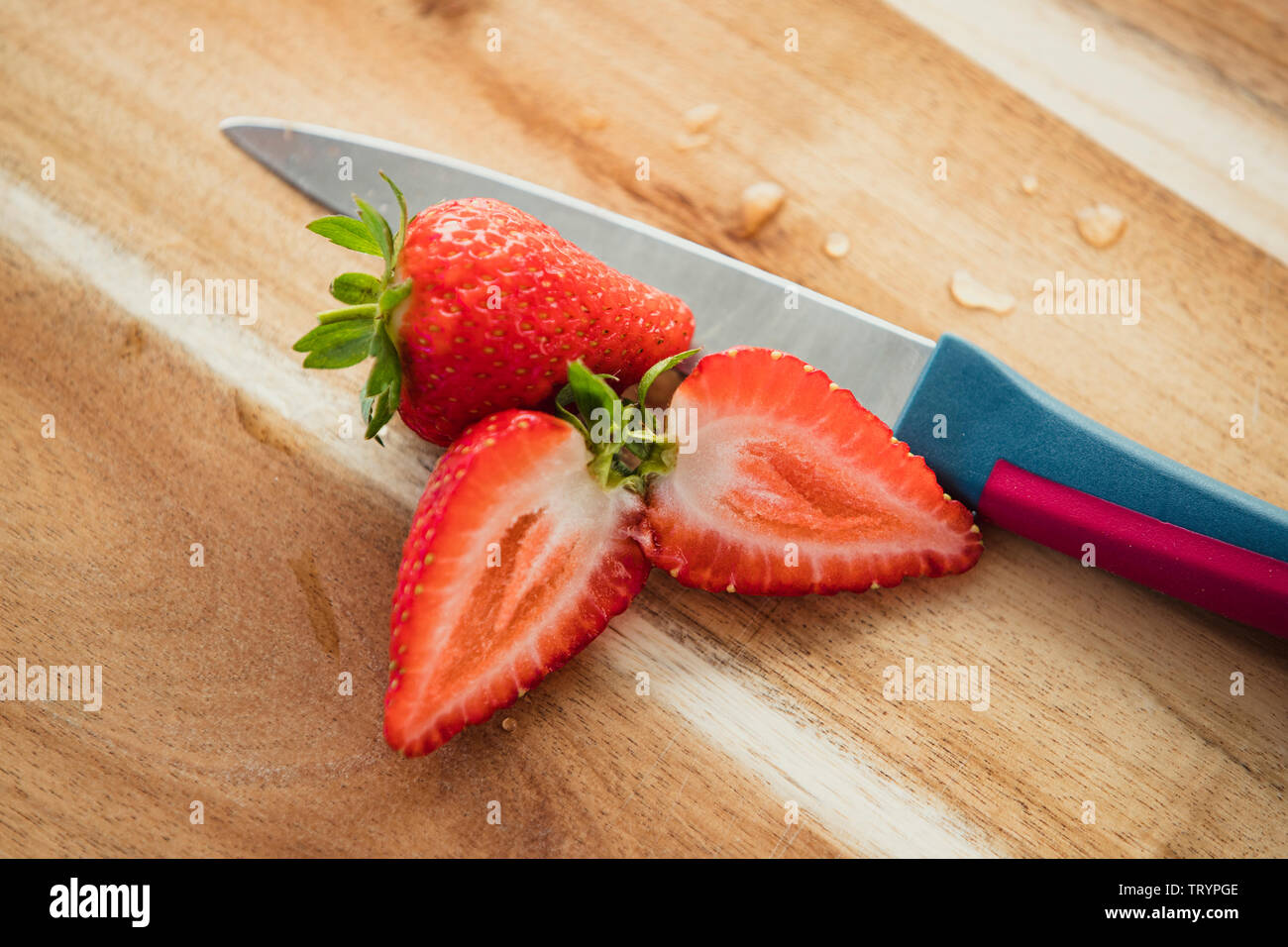 Hohe Betrachtungswinkel von Erdbeeren, in Scheiben geschnitten, auf einer hölzernen Schneidebrett neben einem Messer. Stockfoto