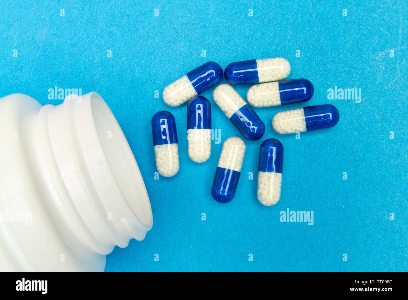 Kapseln, Pillen wurden von einer weißen Flasche auf einem blauen Hintergrund gegossen. Stockfoto