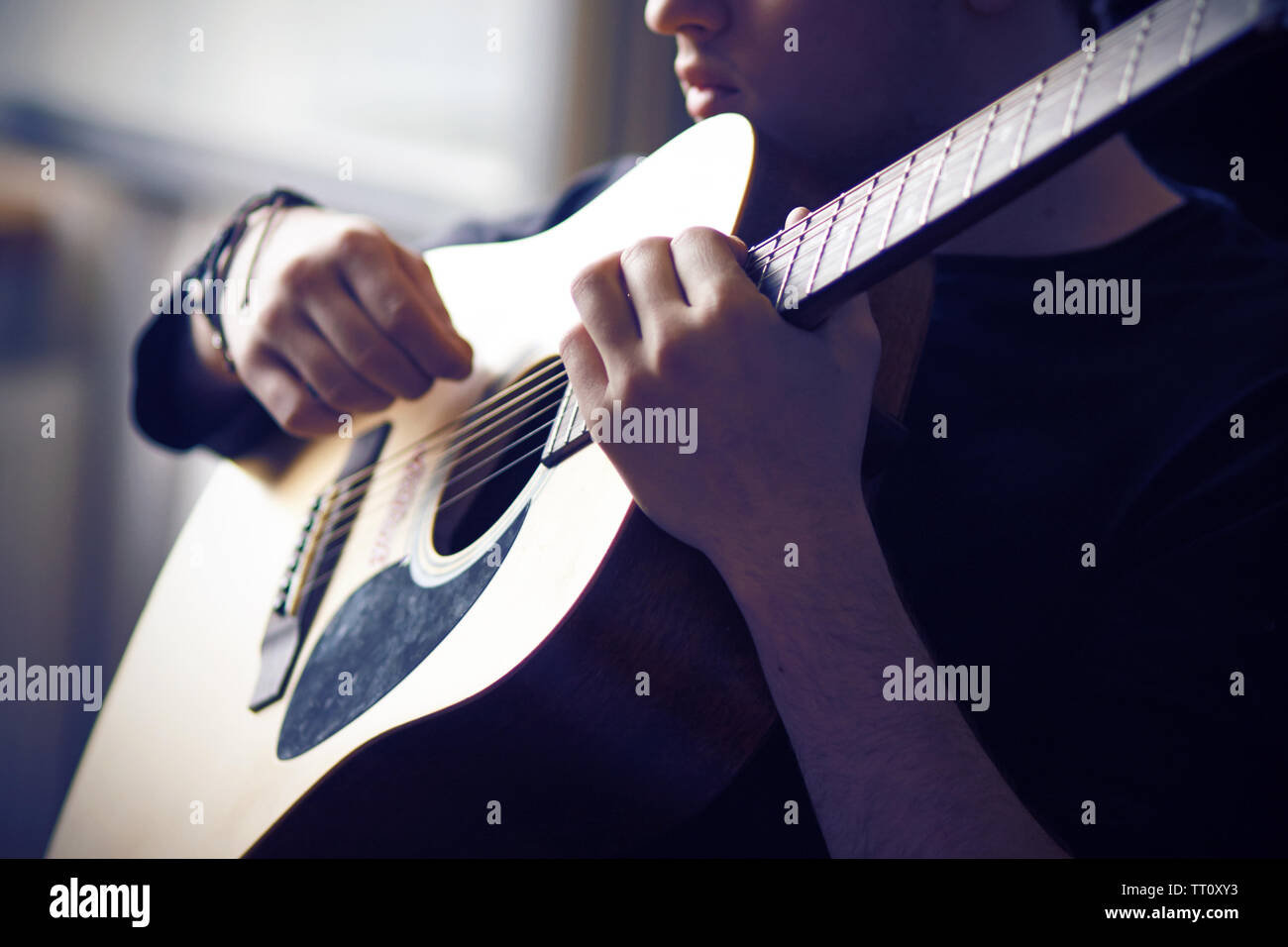 Ein professioneller Musiker in schwarzer Kleidung spielt seine Favorite 6-saitige Gitarre, halten das griffbrett an der Basis und in der Dämmerung. Stockfoto