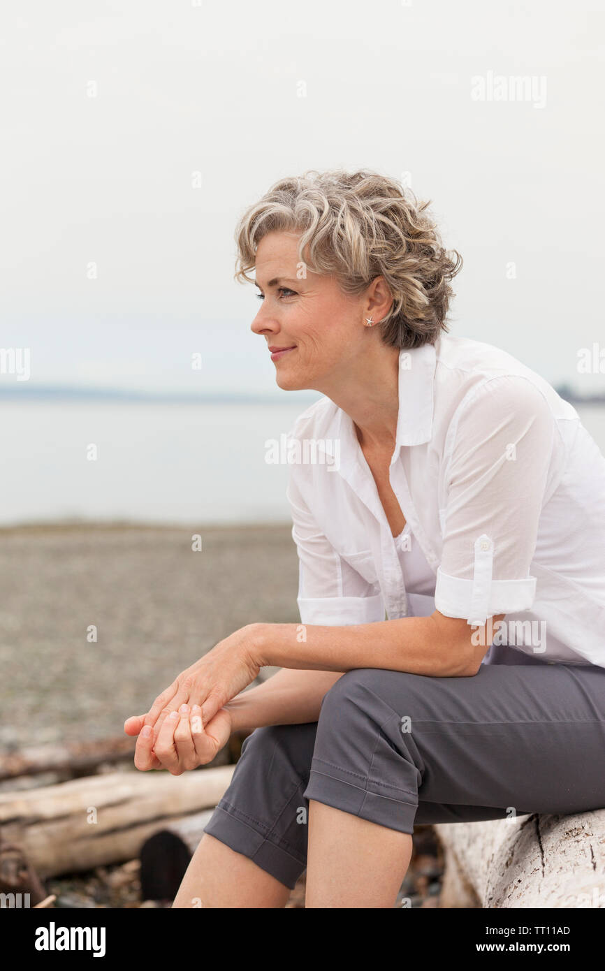 Schöne, glückliche, gesunde, lächelnd, im mittleren Alter, reife Frau sitzen im Freien am Strand Stockfoto