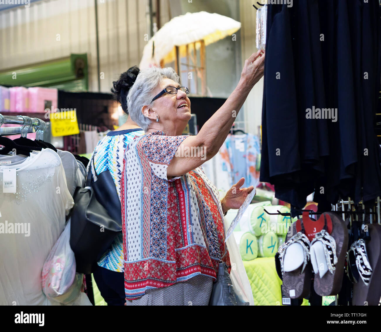 Eine ältere Frau mit grauen Haaren und Brille sieht auf, wie sie für etwas erreicht beim Einkaufen. Land Peddler zeigen Hearne, Texas USA. Stockfoto