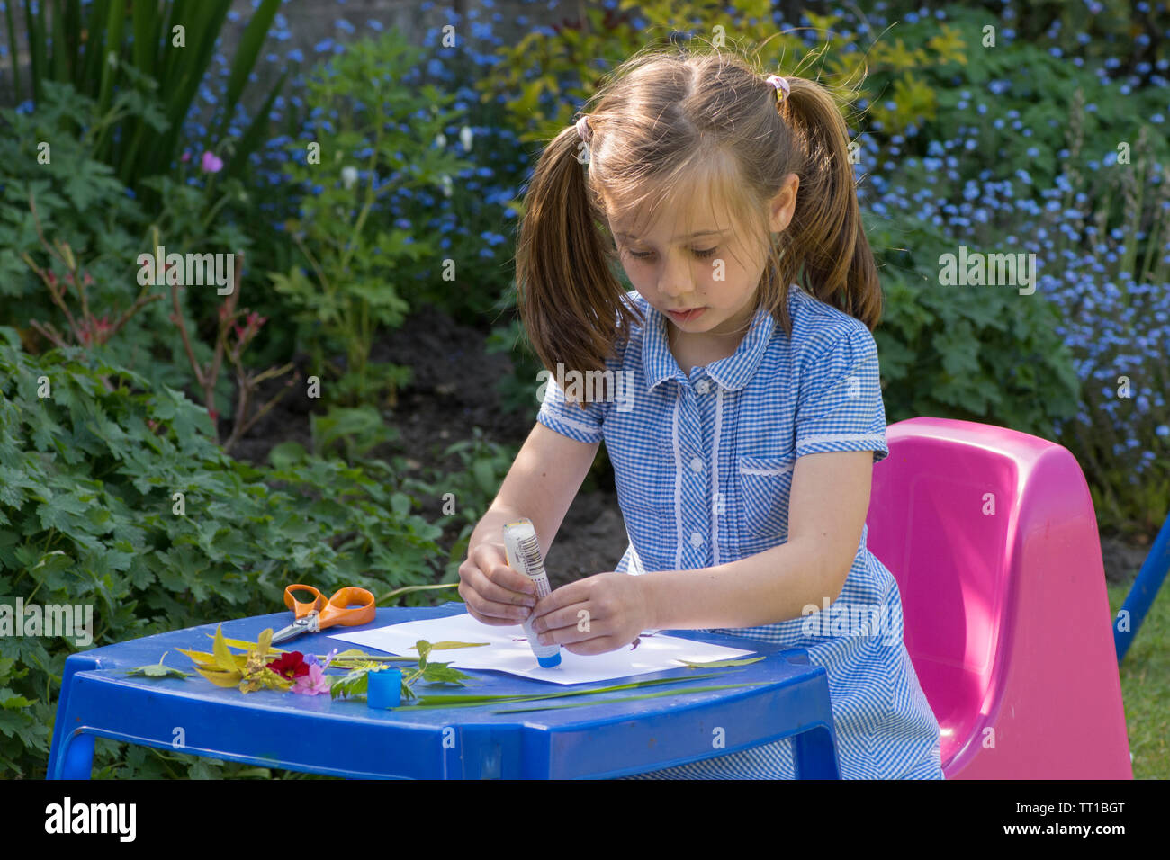 Acht Jahre alten Mädchen in Schuluniform Kleid in den Garten, macht ein Bild von Blumen und Blättern auf Papier geklebt, Natur Kunst Handwerk Stockfoto
