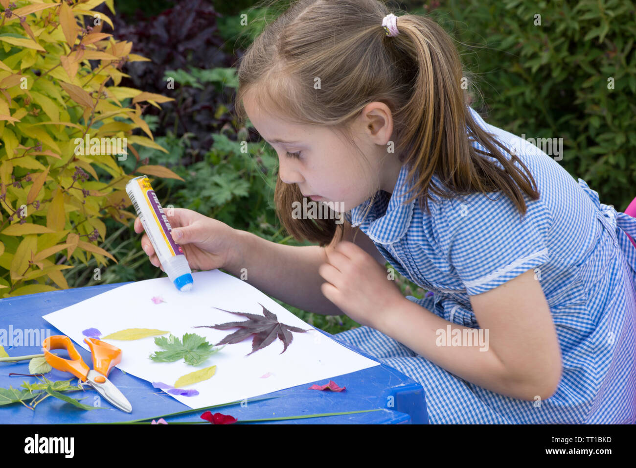 Acht Jahre alten Mädchen in Schuluniform Kleid in den Garten, macht ein Bild von Blumen und Blättern auf Papier geklebt, Natur Kunst Handwerk Stockfoto