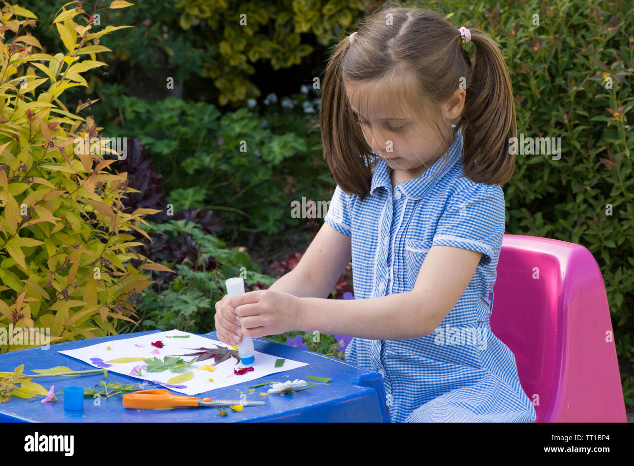 Acht Jahre alten Mädchen in Schuluniform Kleid in den Garten, macht ein Bild von Blumen und Blättern auf Papier geklebt, Natur Kunst Handwerk Stockfoto