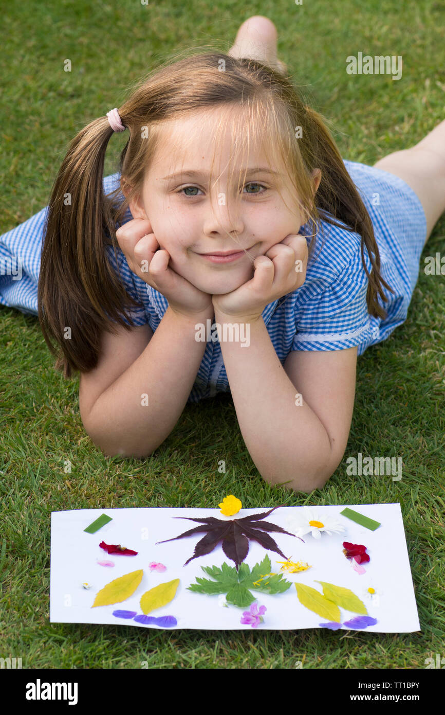 Acht Jahre alten Mädchen in Schuluniform Kleid nach der Schule, im Garten, in dem ein Bild von Blumen und Blättern auf Papier geklebt, Posing, Natur Kunst Handwerk Stockfoto