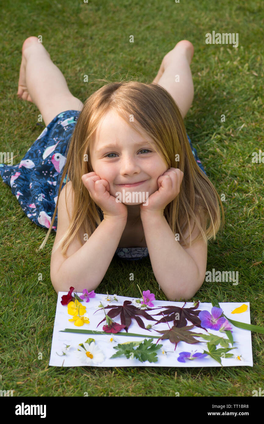 Drei Jahre alte Mädchen mit auf Gras im Garten, durch ein Bild von Blumen und Blättern auf Papier geklebt, Posing, Natur Kunst Handwerk, schauen, glücklich Stockfoto