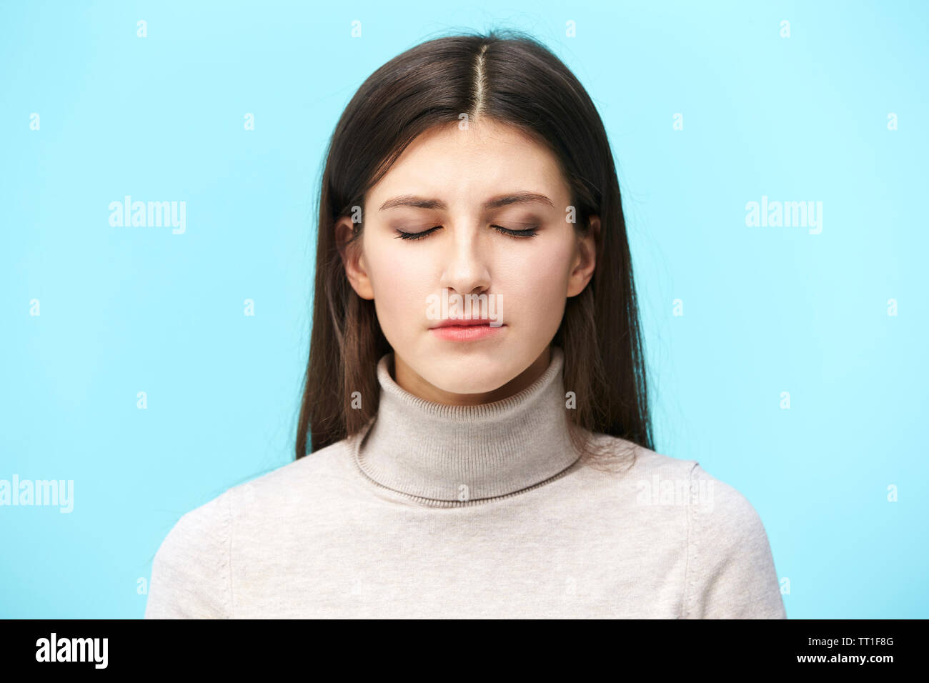 Portrait einer jungen kaukasischen Frau, die Augen geschlossen, auf blauem Hintergrund isoliert Stockfoto