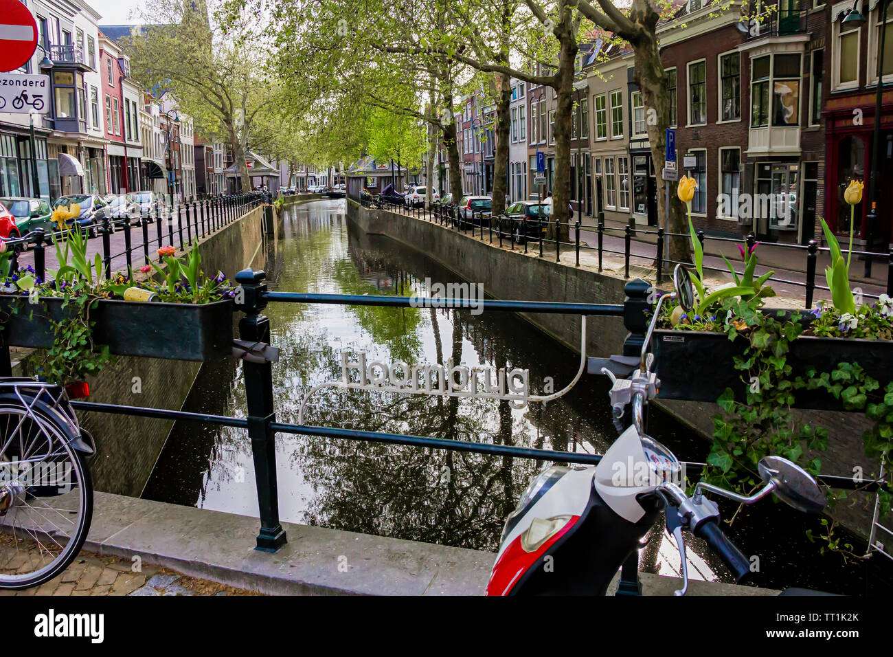 Gouda, Holland, Niederlande, April 23, 2019, Fahrräder und in der Nähe einer Brücke entlang einer Straße geparkt, Canal in Gouda Altstadt. Blumen in einem blumenbeete, Boot Stockfoto