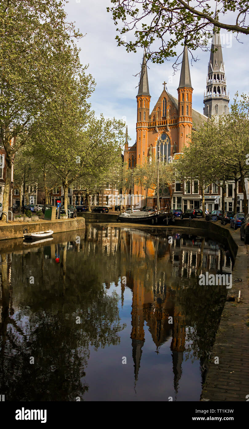 Gouda, Holland, Niederlande, April 23, 2019, Gouwekerk Kirche in der Nähe einer Brücke an einem Kanal in Gouda Altstadt. Blumen in einem parterres, Boot auf dem Wasser. Stockfoto