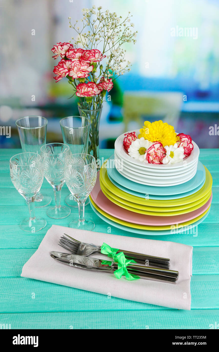 Stapel bunter Keramik Geschirr und Blumen, auf Holztisch, auf hellen Hintergrund Stockfoto