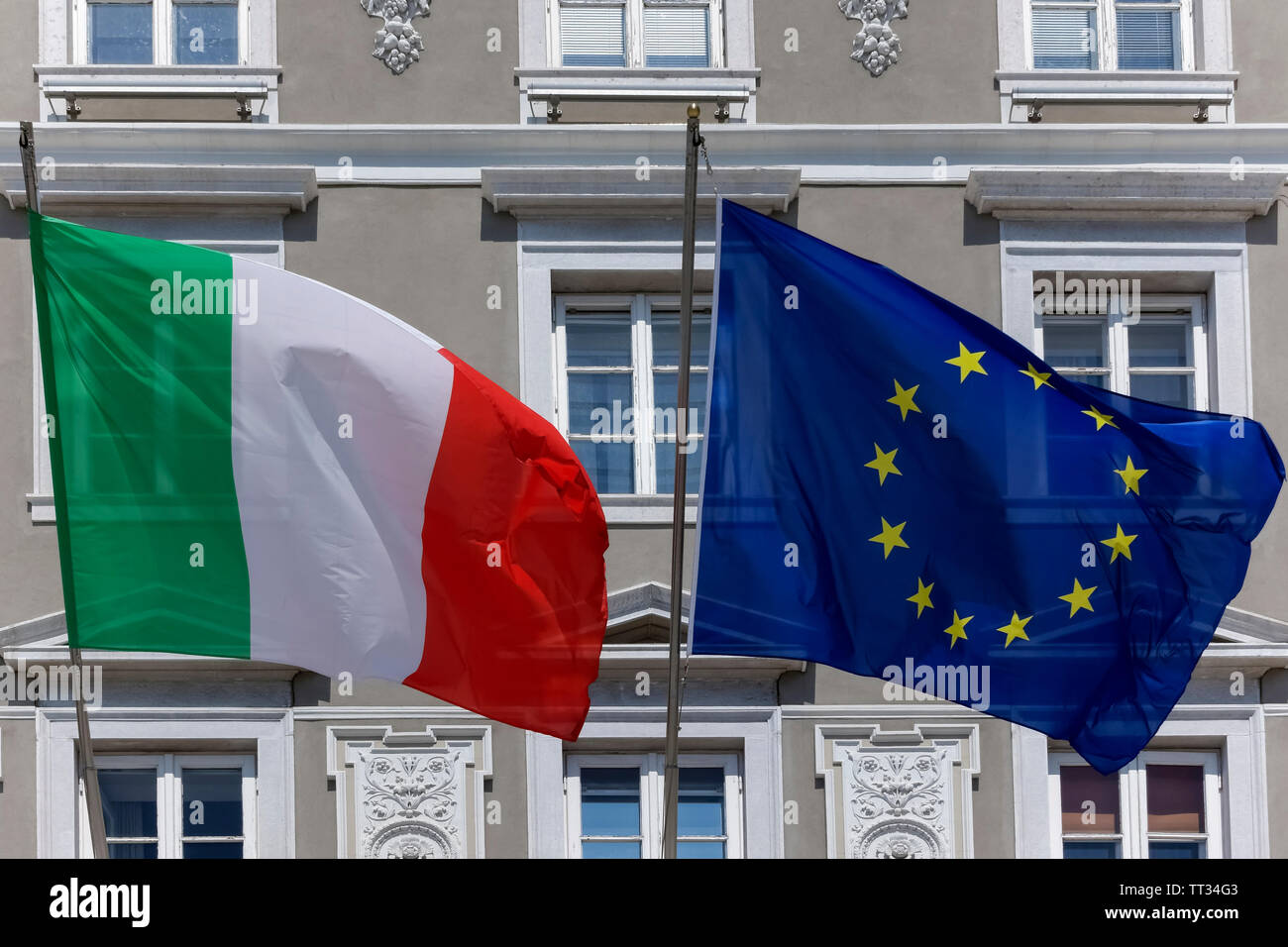 Vor der Fassade des Palazzo Stratti auf der Piazza dell'Unità d'Italia in Triest, Italien, Europa und der EU winken italienische und europäische Flaggen. Stockfoto