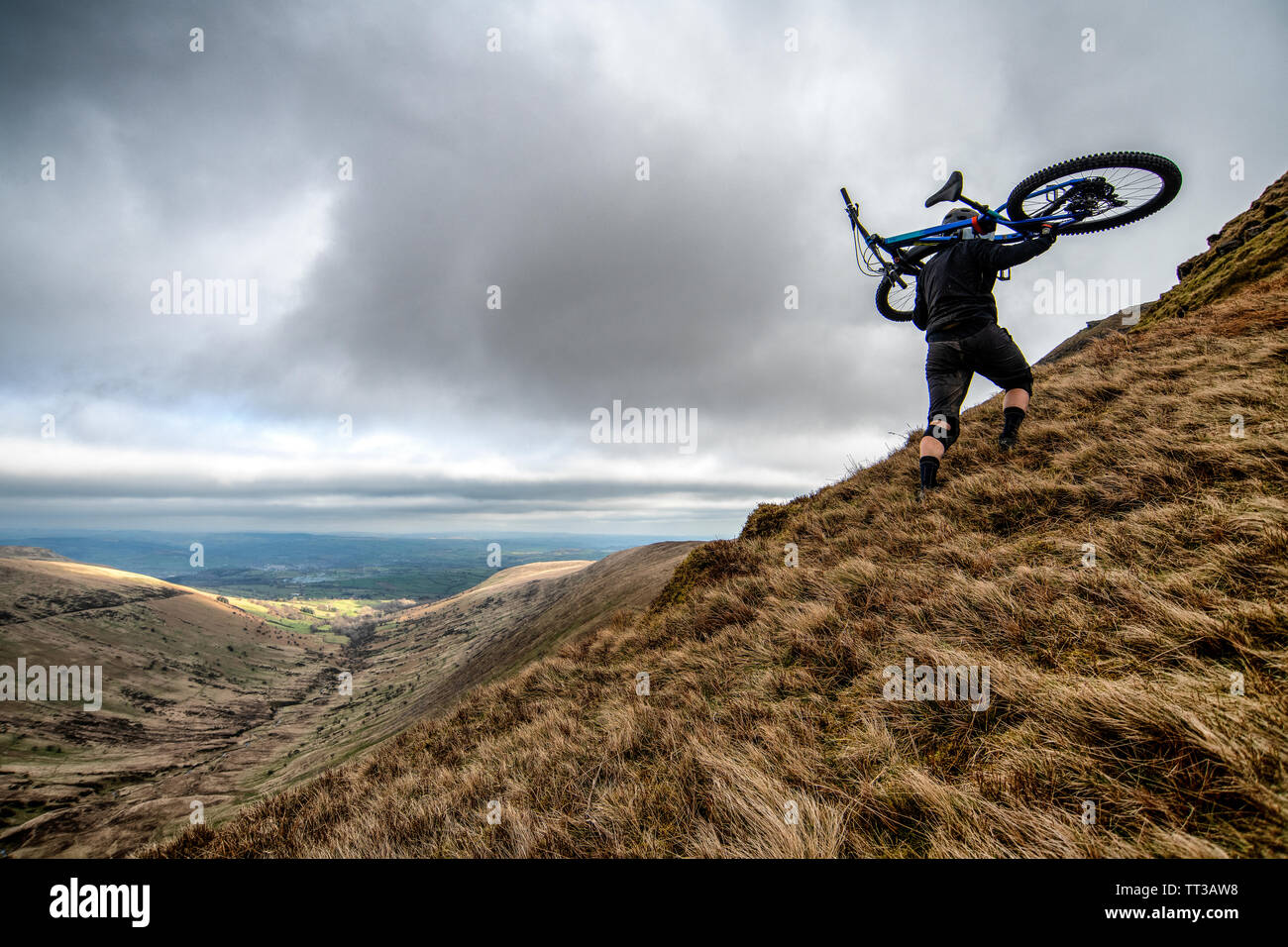 Ein Mann trägt ein Mountainbike auf seinen Schultern zum Gipfel der Lüfter-y-Groß in den Brecon Beacons National Park, Wales. Stockfoto