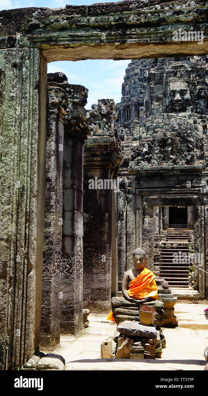 Eingang des schönen Bayon Tempel - mit einem Buddha Statue in orange Tuch in der Mitte sitzen, die von zerstörten Säulen und einem alten Stein umgeben Stockfoto
