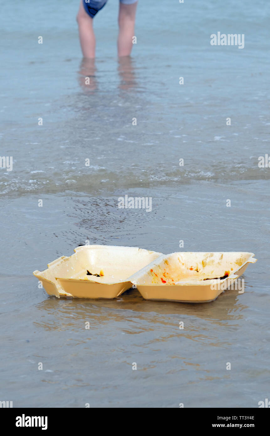 Müll schwebend an einem Strand mit Beine einer Person Paddeln im Hintergrund Stockfoto