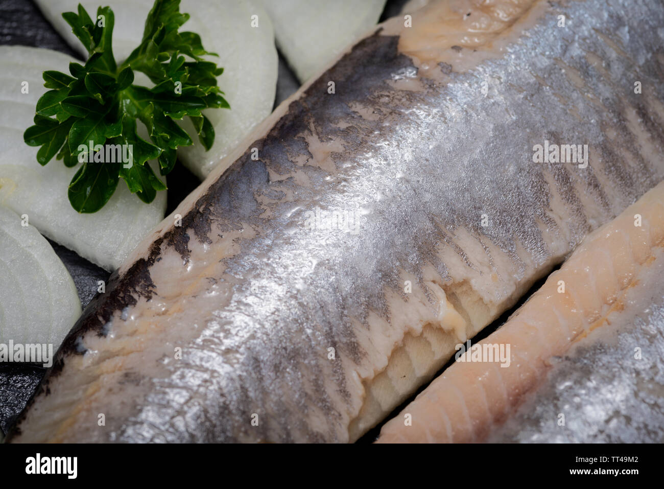 Leckere gesalzene Heringe, garniert mit Gelbe Zwiebel und frischer Petersilie. Natürliche schwarze Stein. Clupea harengus festgelegt. Stockfoto