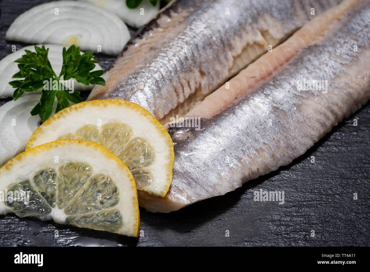 Gesalzene Heringsfilets ohne Knochen garniert mit Zitronenscheiben und frischer Petersilie. Natürliche schwarze Stein. Clupea harengus festgelegt. Stockfoto