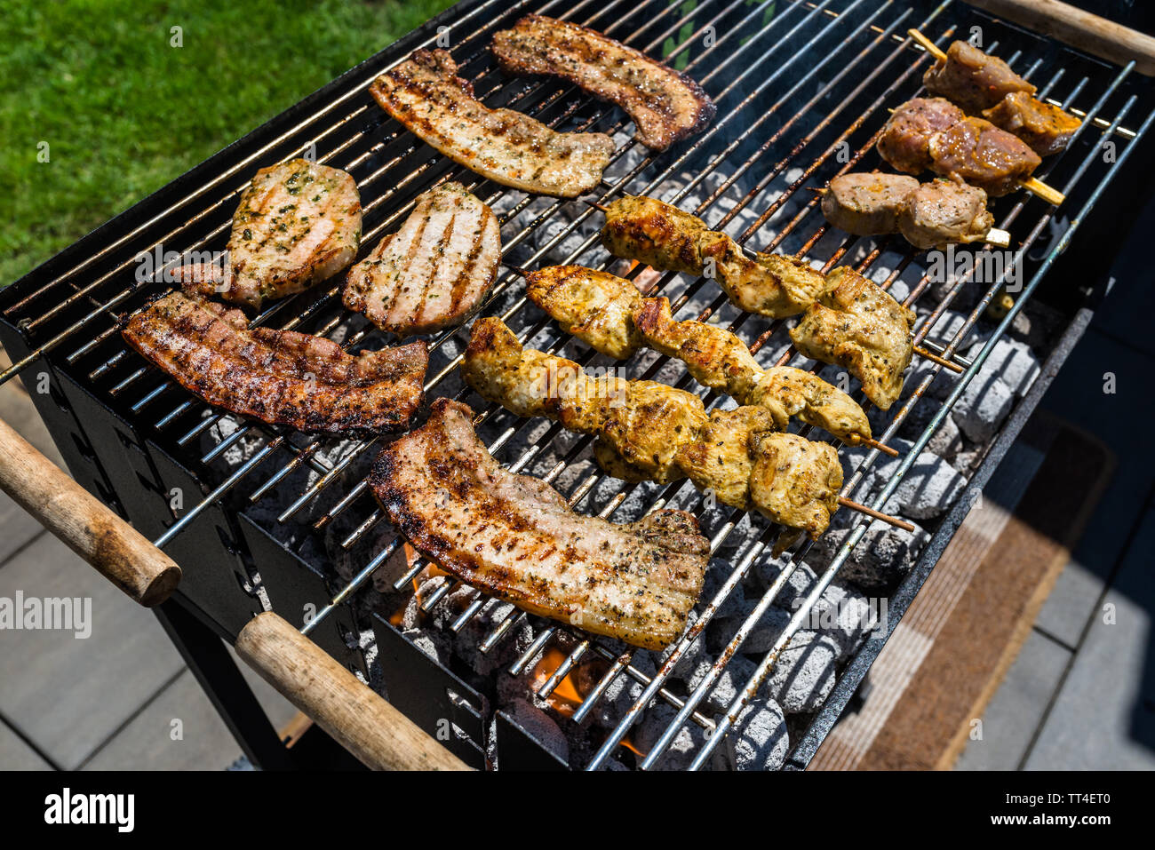 Verschiedene Arten von Fleisch gebraten auf der Startseite Grill, stehend auf einem Haus Garten auf den Pflasterstein. Stockfoto