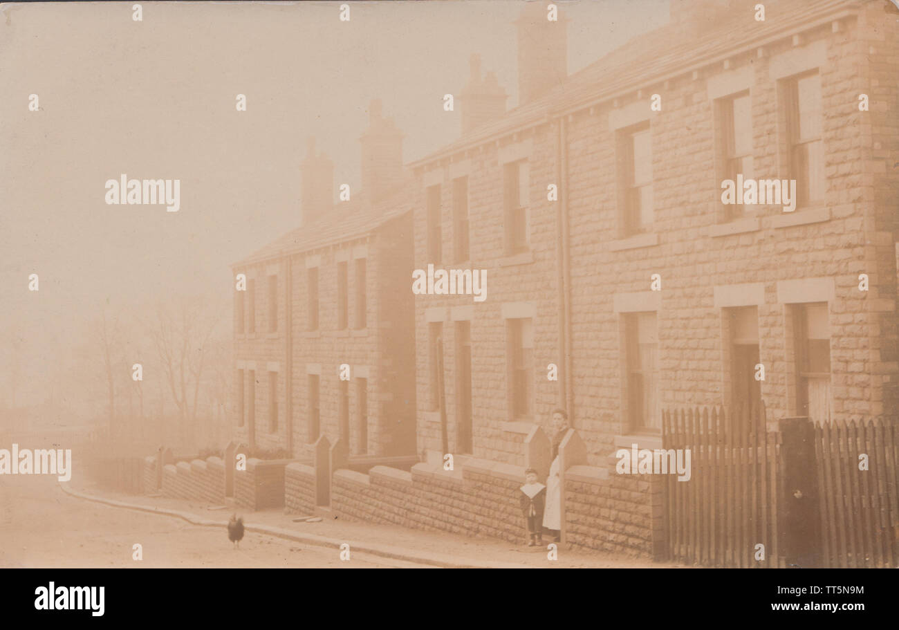 Jahrgang fotografische Postkarte zeigt einige Bewohner außerhalb einer Reihe von Reihenhaus und Doppelhaus Häuser in einer britischen Straße im frühen 20. Jahrhundert. Stockfoto
