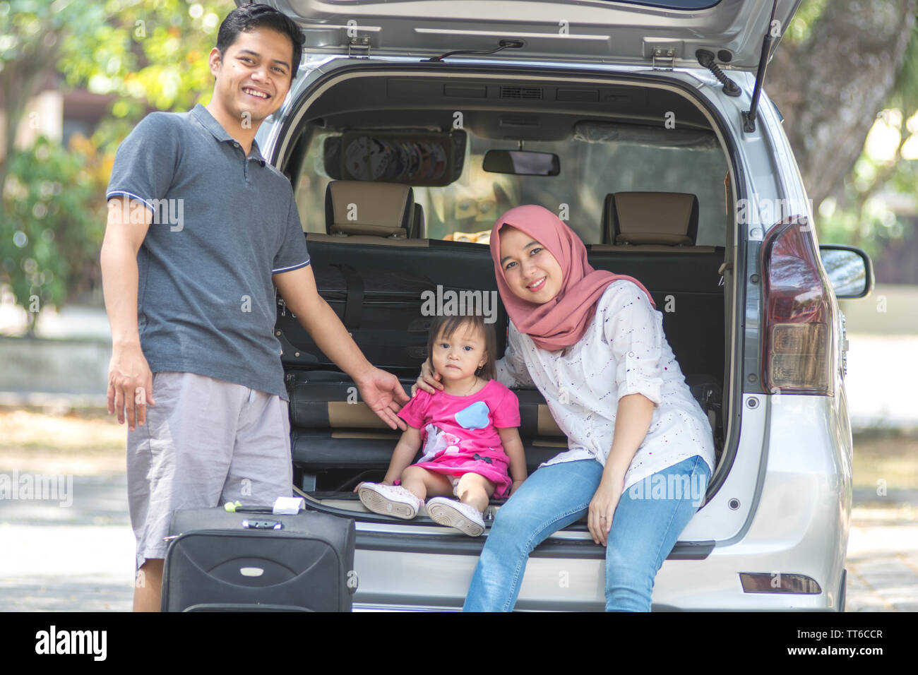 Junge muslimische Familie, Verkehr, Freizeit, Reise und Personen Konzept - glückliche Mann, Frau und kleines Mädchen sitzen auf Kofferraum der Limousine Auto und talkin Stockfoto