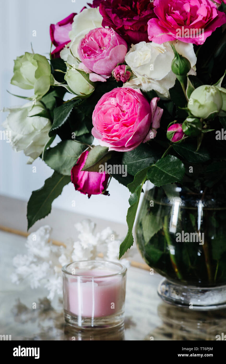 Weibliche Innenraum - Bouquet von duftenden, pinkfarbenen und weißen Englischen Rosen, Muscheln und rosa Kerze auf den Glastisch Stockfoto