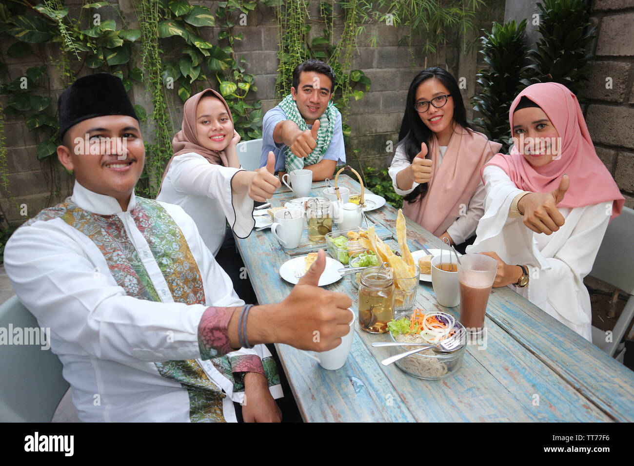 Gruppe der glückliche junge muslimische Abendessen im Freien givung Daumen bis zu Kamera während des Ramadan feiern, brechen das Fasten Stockfoto
