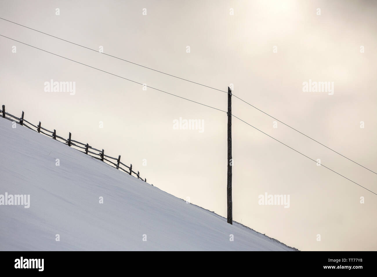 Winterlandschaft. Steilen Berghang mit elektrischen Strom Linie auf Kopie Raum Hintergrund der weiße Schnee und hellen Himmel. Stockfoto