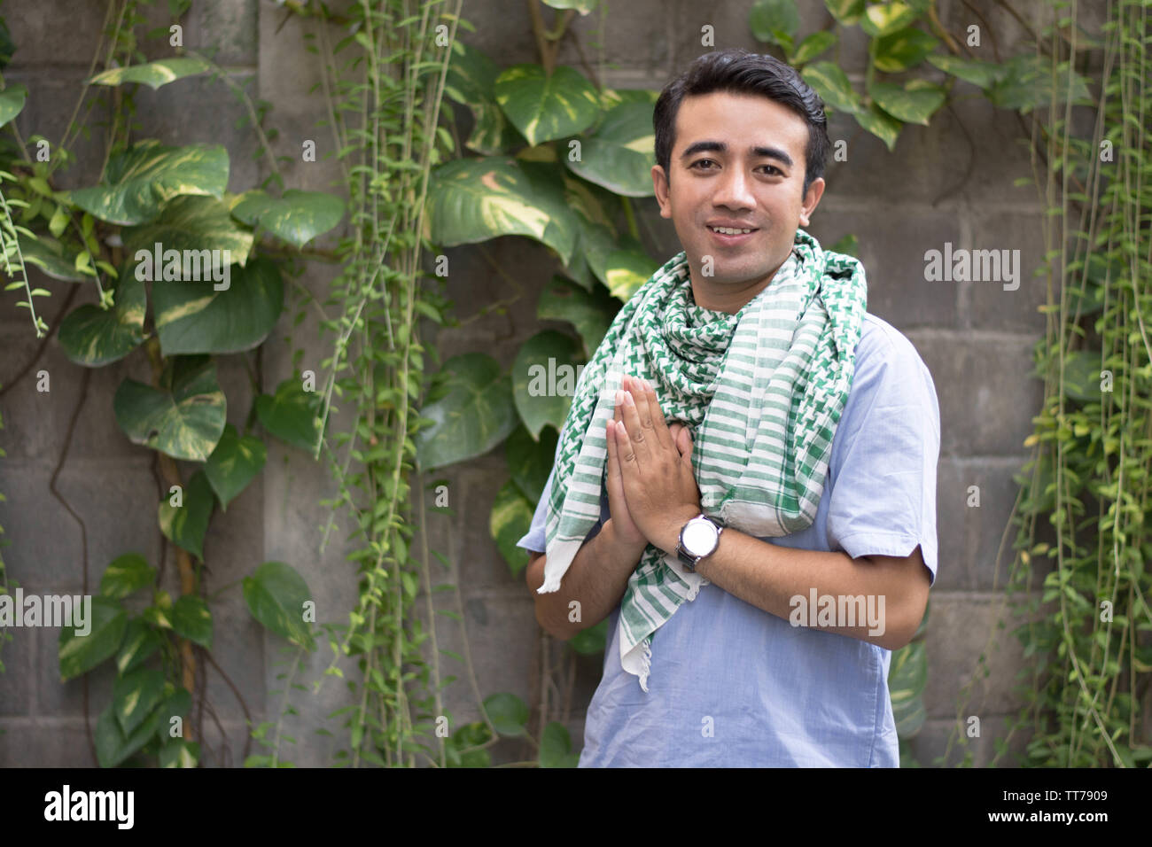 Porträt EINES muslimischen Mannes stehen und posieren vor Der Kamera im Außenbereich mit Pflanzenbaum und Blatt dahinter Stockfoto