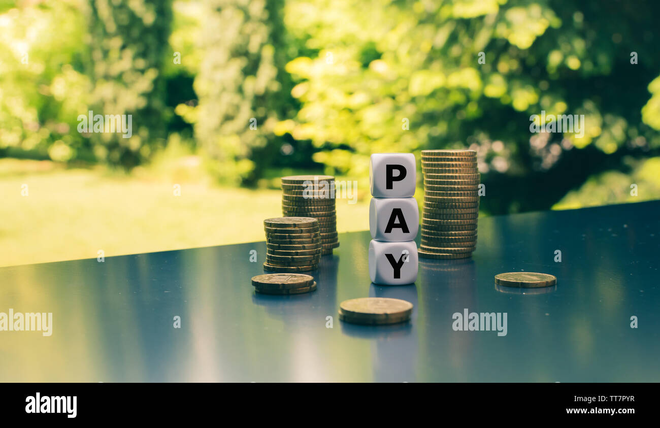 Würfel Form das Wort "Bezahlen" neben Stapeln von Münzen. Stockfoto