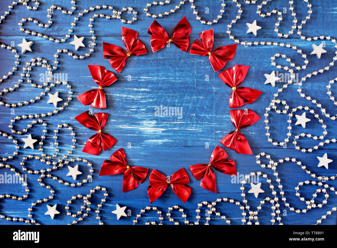 Weihnachtsdekoration mit einem cirle der roten Bändern, Silber Perlen Kette und Sterne auf dunkelblauem Hintergrund Holz - Platz für Text Stockfoto