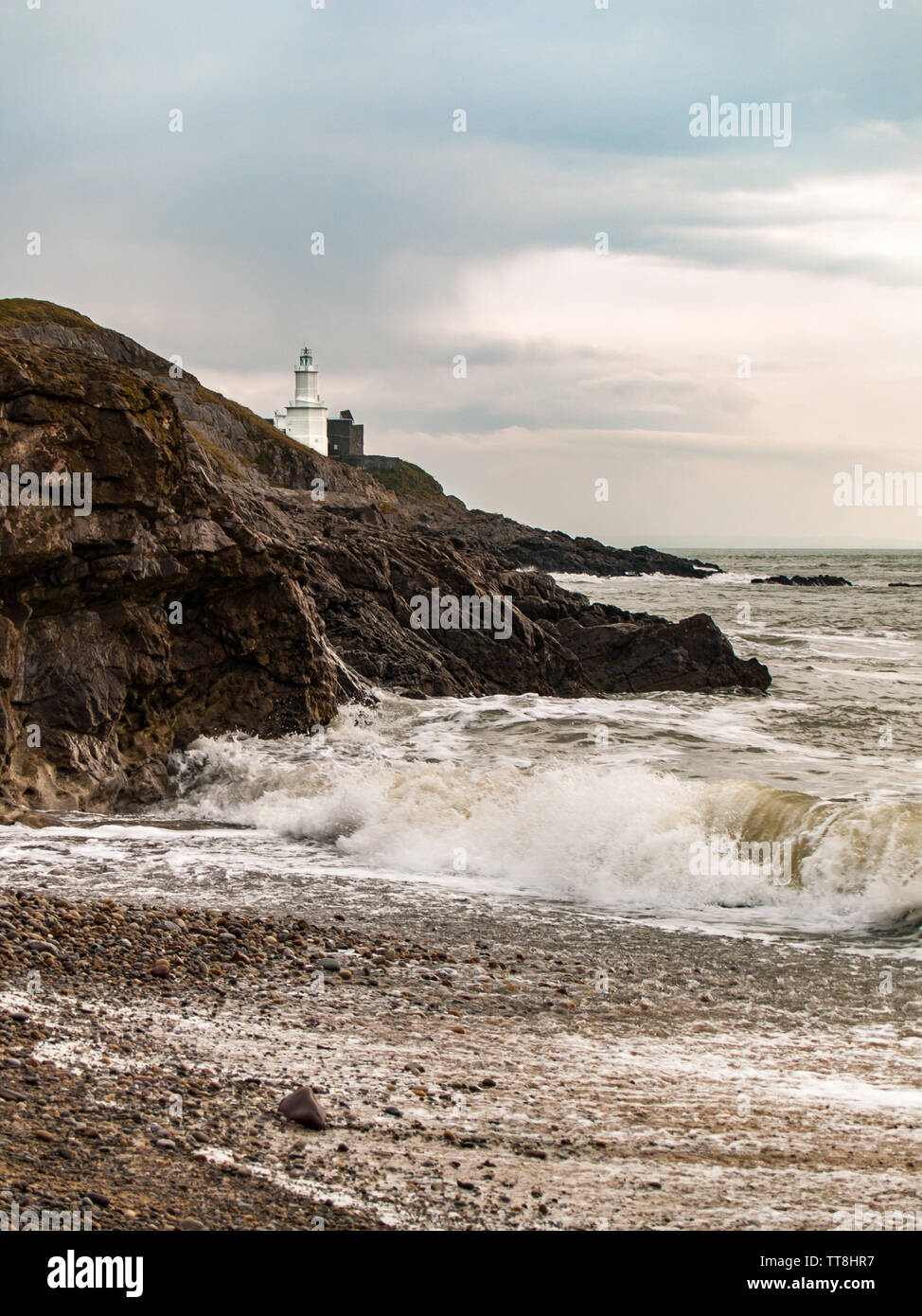 Leuchtturm auf mumbles Mumbles Head als von Armband Bucht mit Wellen auf den Strand gesehen. Swansea, Gower, Wales, UK. Stockfoto