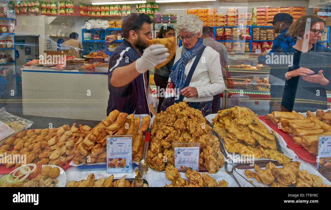 LONDON ENGLAND BRICK LANE indisches Essen SCHAUFENSTER MIT KUNDEN KAUFEN PFLANZLICHE SAMOSAS Chicken Tikka und CHANNA ROLLEN Stockfoto