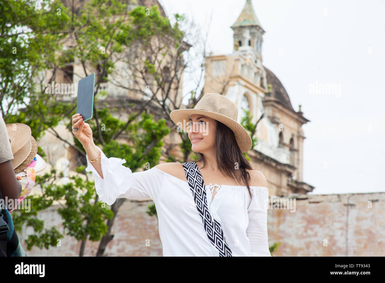 Schöne junge Frau, die versucht, auf die Hüte, die man von einem Straßenhändler in Cartagena de Indias zu kaufen ummauerten Stadt Stockfoto