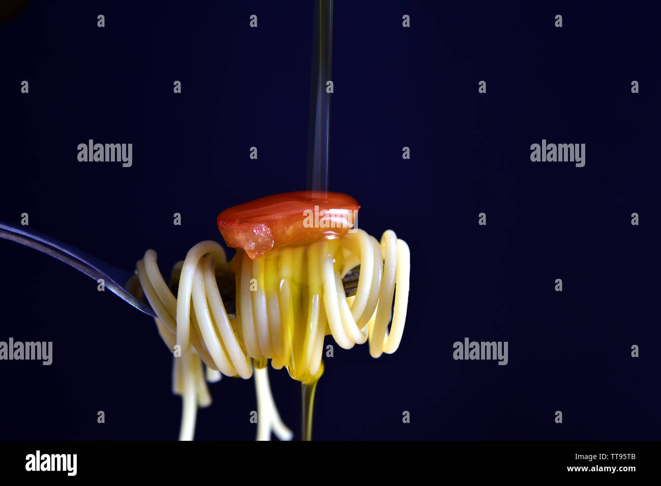 Nahaufnahme einer Gabel mit Pasta, Tomaten und Olivenöl gegen einen dunklen Hintergrund Stockfoto