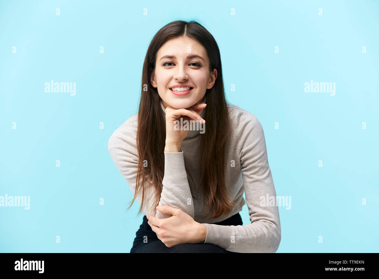 Porträt einer schönen jungen kaukasischen Frau, glücklich und lächelnd, Kamera, Hand am Kinn, auf blauem Hintergrund isoliert Stockfoto