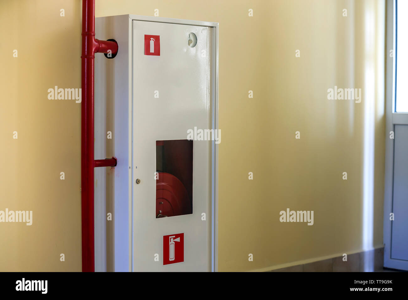 Weiß Metallschrank mit Feuerlöschanlagen schlauchhaspel an der Wand Kopie Raum Hintergrund. Stockfoto