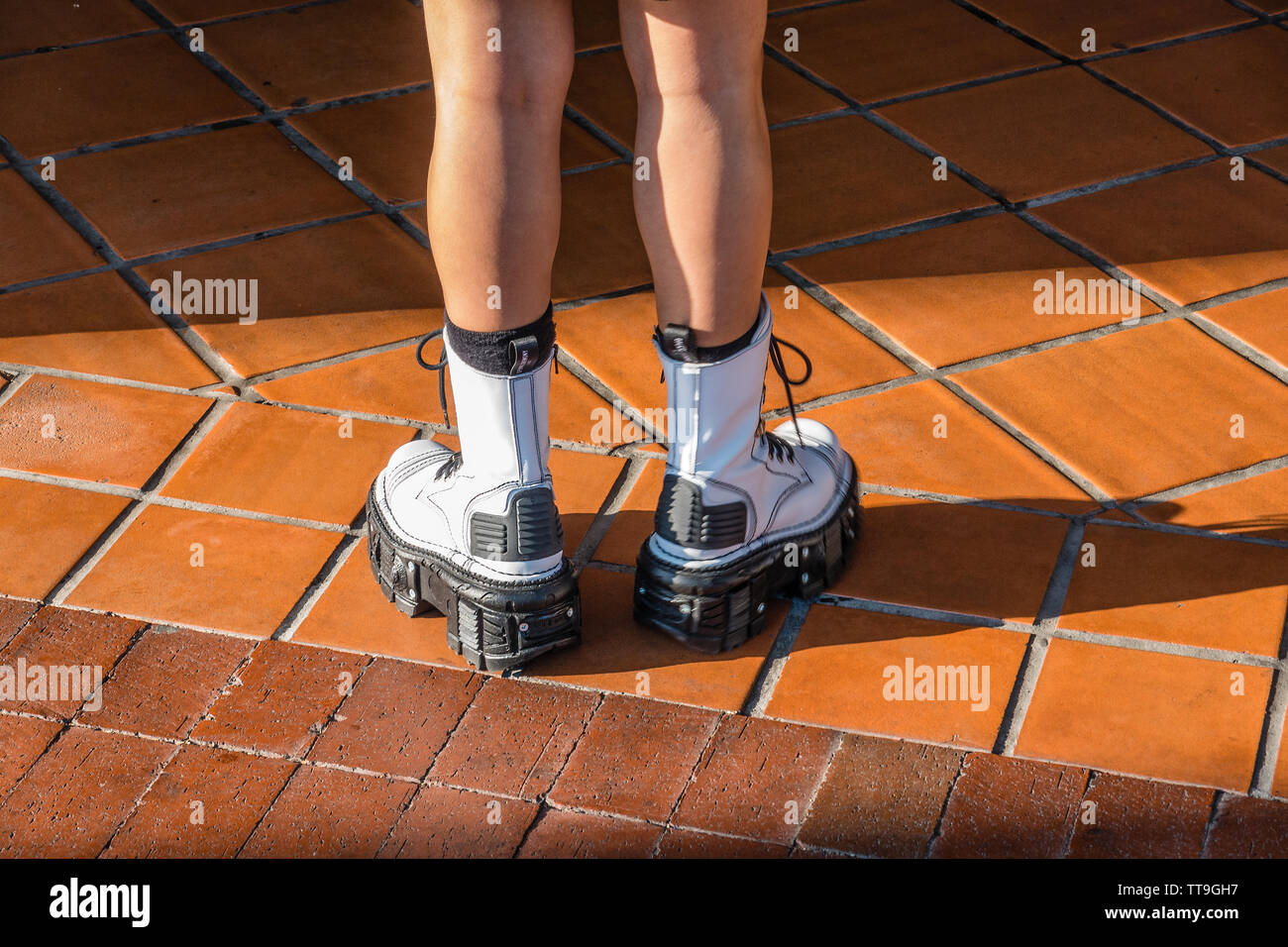 Eine Nahaufnahme der Beine und Schuhe von einem jungen weiblichen Erwachsenen mit schwarzen und weißen hohe Plattform schicke Schuhe in ein modisches Statement steht auf roten Fliesen. Stockfoto
