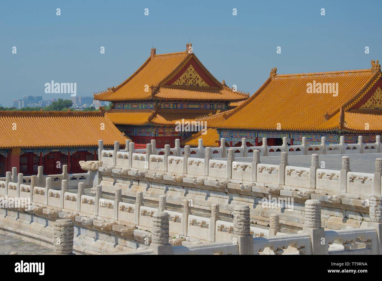 Reihen von weißen Marmor verzierten Säulen im Vordergrund, vor der hellen orange Dächer der traditionellen chinesischen Gebäuden gegen den blauen Himmel Stockfoto