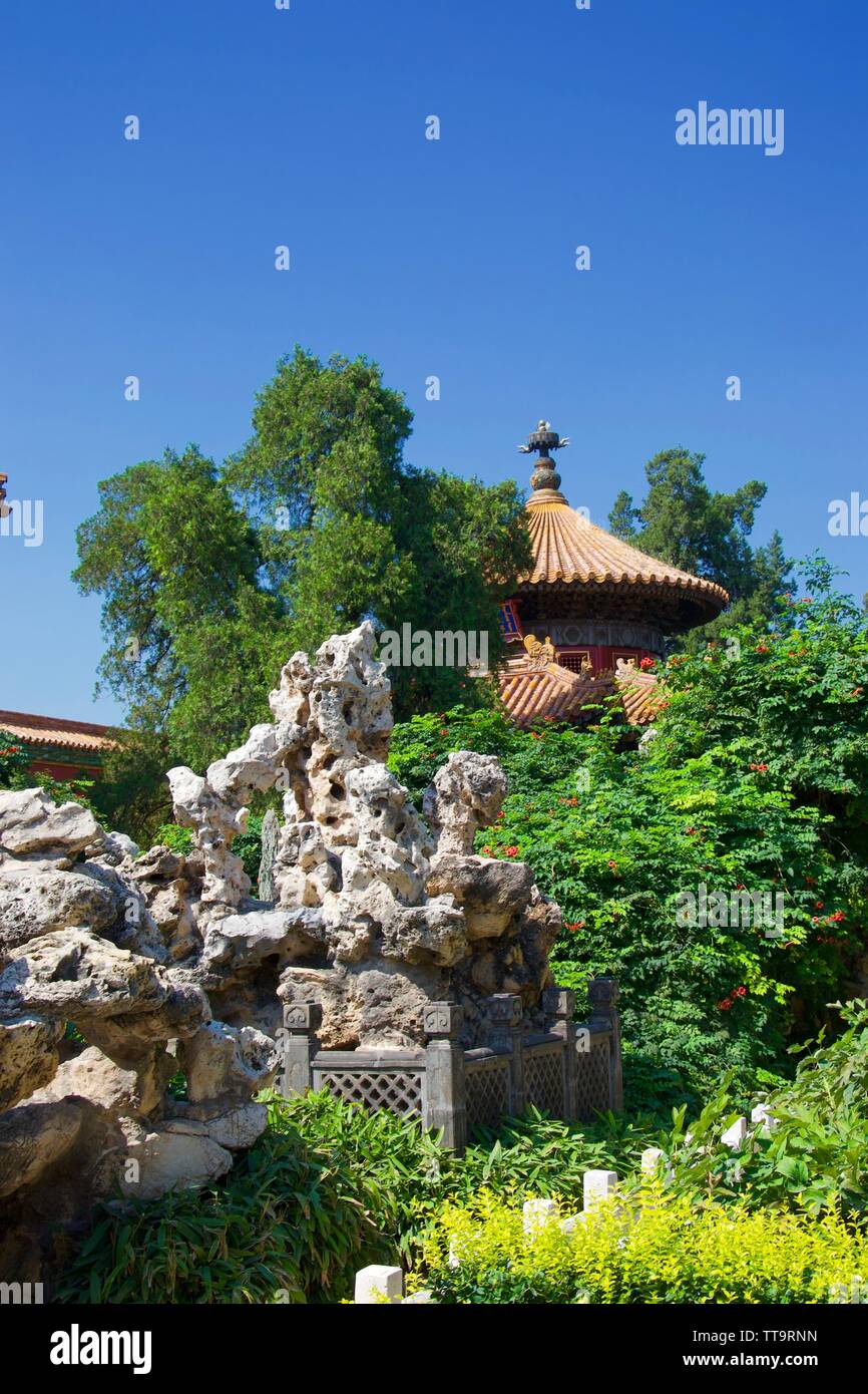 Der Sonnenbeschienenen Steingarten und Baum im Vordergrund, mit dem Dach eines traditionellen chinesischen Tempel (Pagode) hinter der helle grüne, üppige Bäume und vor einem Stockfoto
