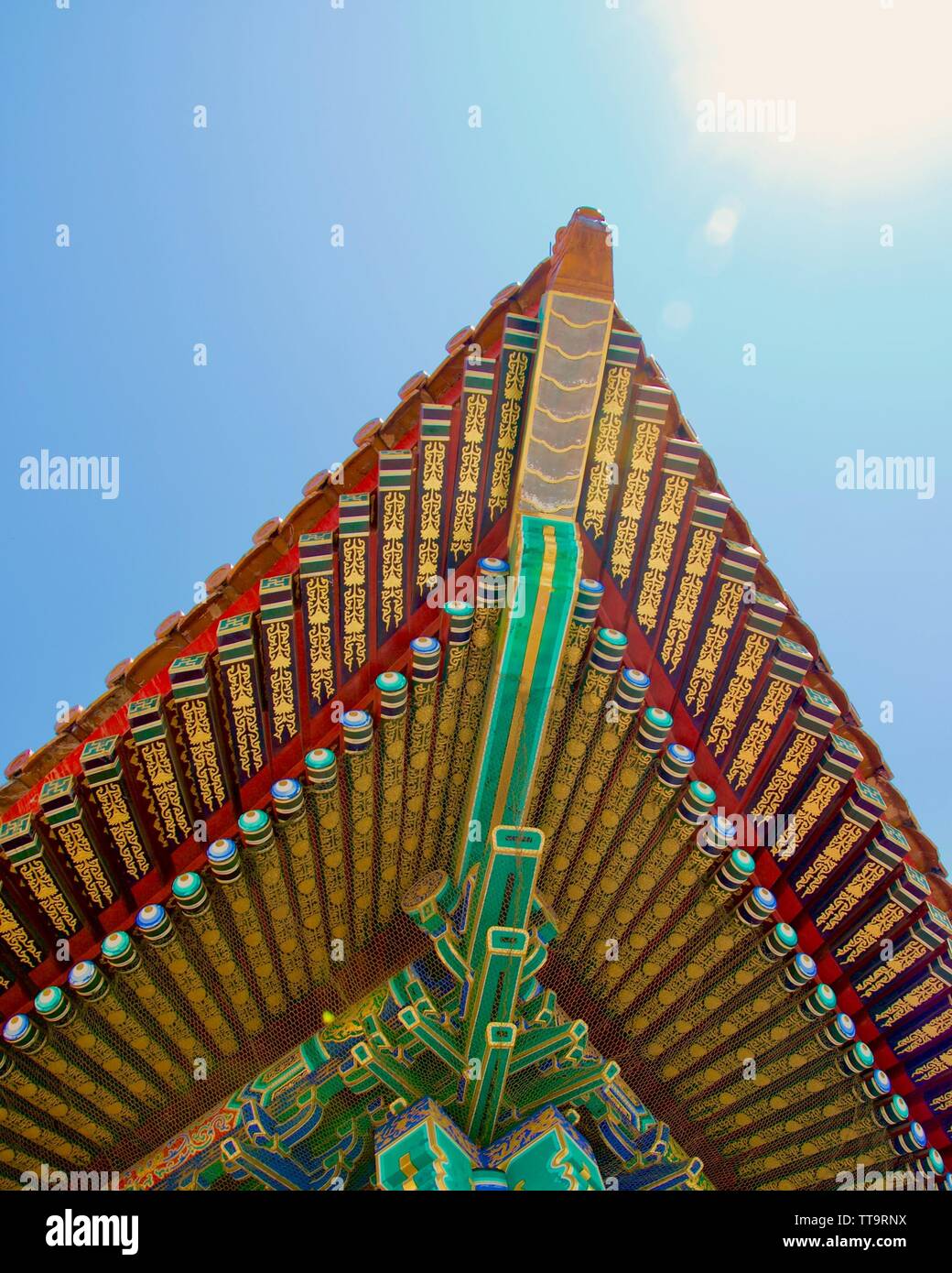 Schauen oben an der Ecke des Daches eines traditionellen chinesischen Gebäude; blauer Himmel und strahlende Sonne. Die Farben sind leuchtend und strahlend: Gold, Grün Stockfoto