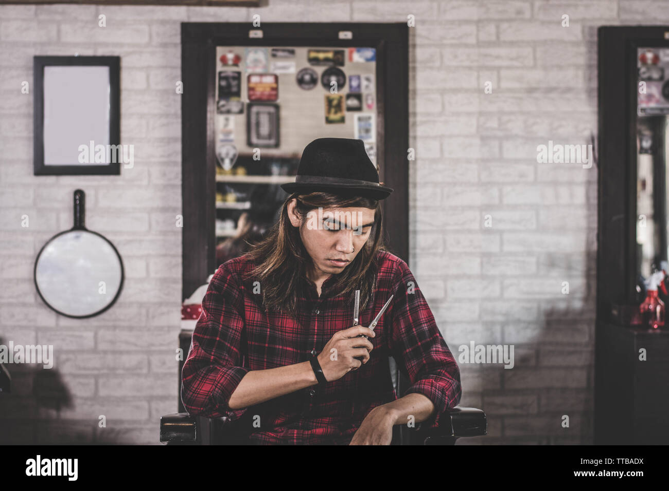 Portrait von selbstbewussten jungen lange Friseur Friseur im Vintage barbershop Stuhl halten zwei scissor konfrontiert und Suchen von der Kamera sitzen Stockfoto