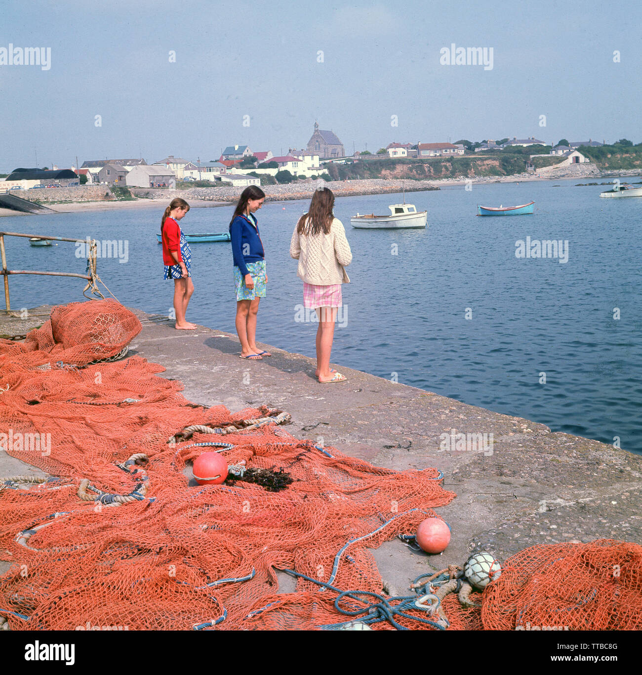 1960, historische, drei junge Mädchen im Teenageralter durch Fischernetze an den Rand des Wassers am Hafen in Kilmore, einem Fischerdorf in der Grafschaft Wexford, Irland. Stockfoto