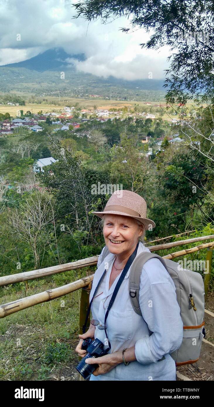 Lächelnde ältere weibliche Reisende mit der Kamera in der spektakulären Landschaft Stockfoto