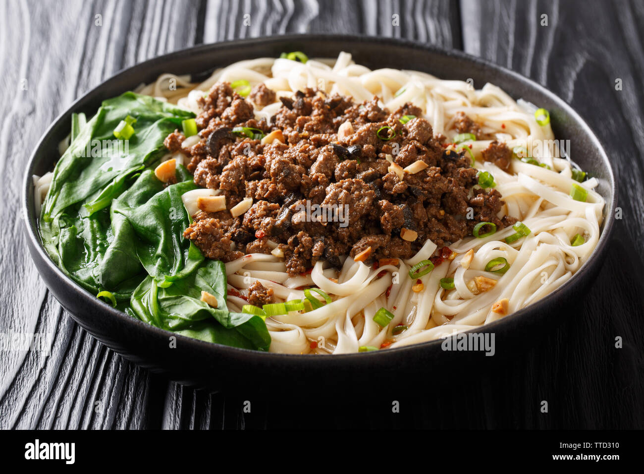 Würzige Dan Dan Nudeln mit Hackfleisch und Kräutern mit heißer Soße in einem Teller auf dem Tisch. Horizontale Stockfoto
