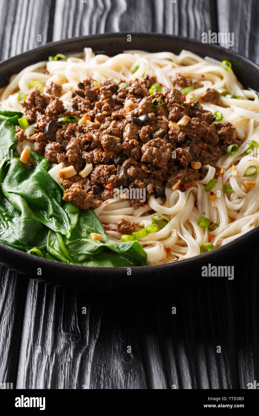 Dan Dan Nudeln - herzhaft und würzig Sichuan Nudeln serviert mit Hackfleisch Nahaufnahme auf dem Teller auf dem Tisch. Vertikale Stockfoto