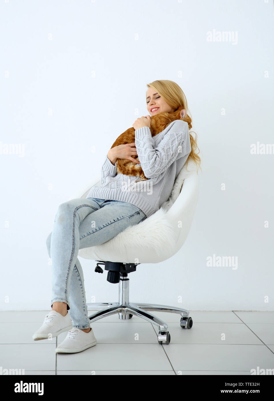 Junge Frau mit roten Katze sitzt auf Stuhl gegen weißen Hintergrund Stockfoto