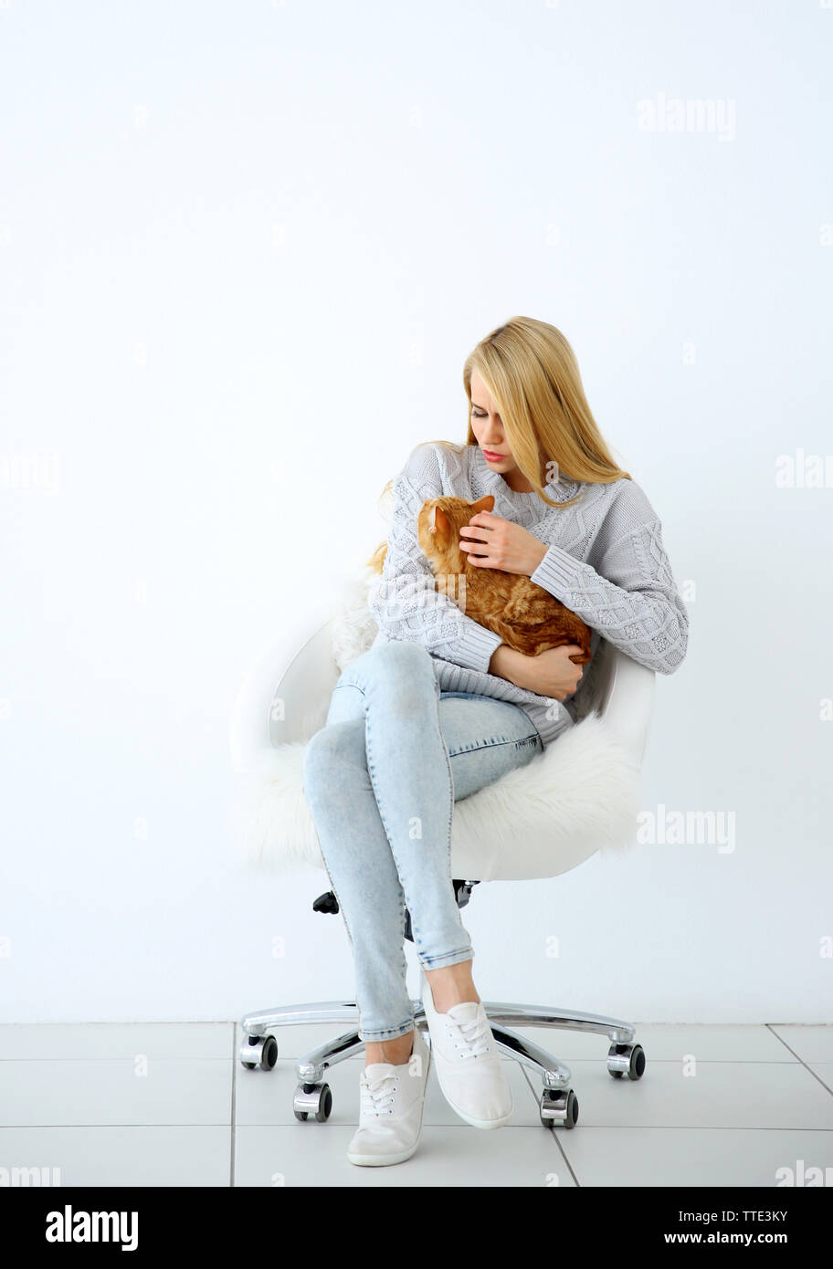 Junge Frau mit roten Katze sitzt auf Stuhl gegen weißen Hintergrund Stockfoto